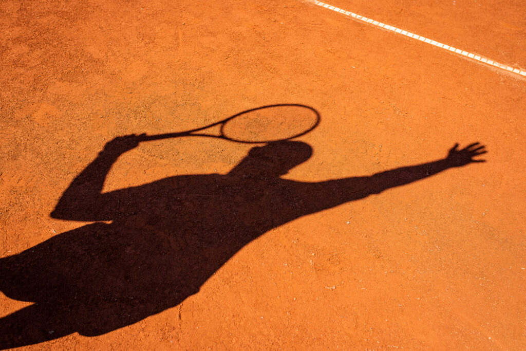 Schatten eines Tennisspielers beim Aufschlag auf Sandplatz