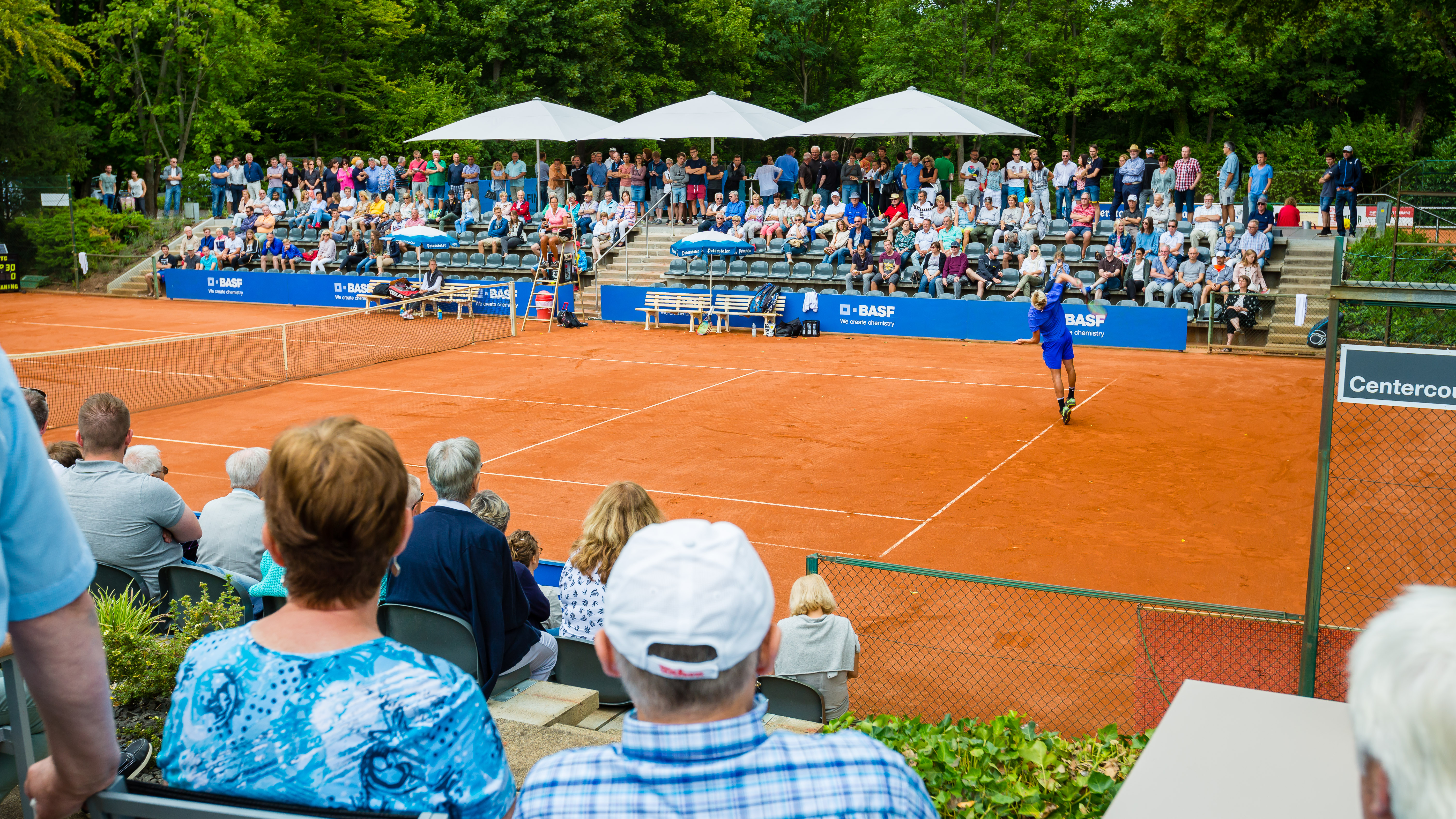 Tennisspiel auf Sandplatz vor Zuschauern
