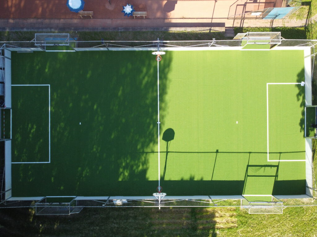 Luftaufnahme eines grünen Fußballplatzes mit Basketballkörben