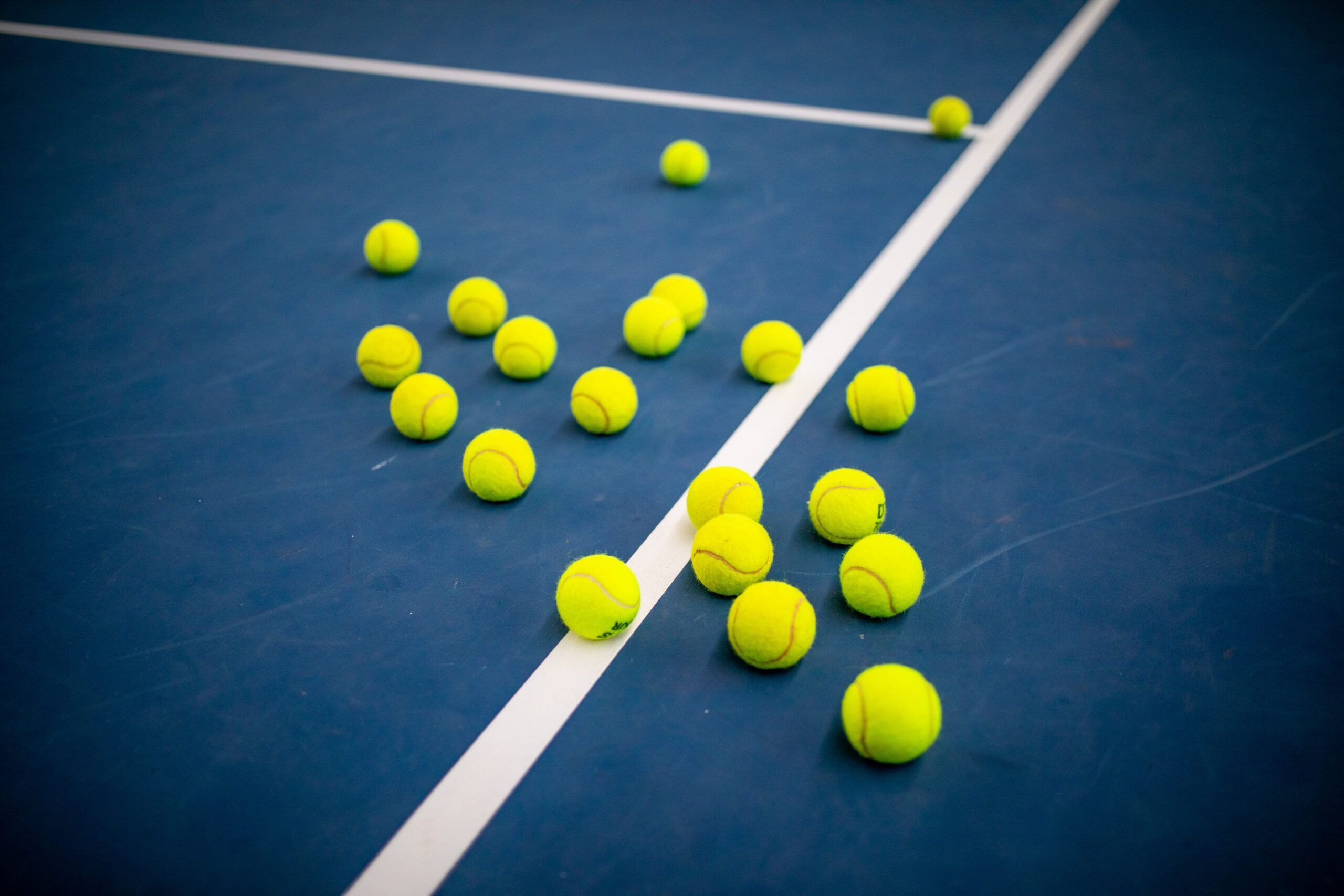 Tennisbälle auf blauem Tennisplatz verstreut