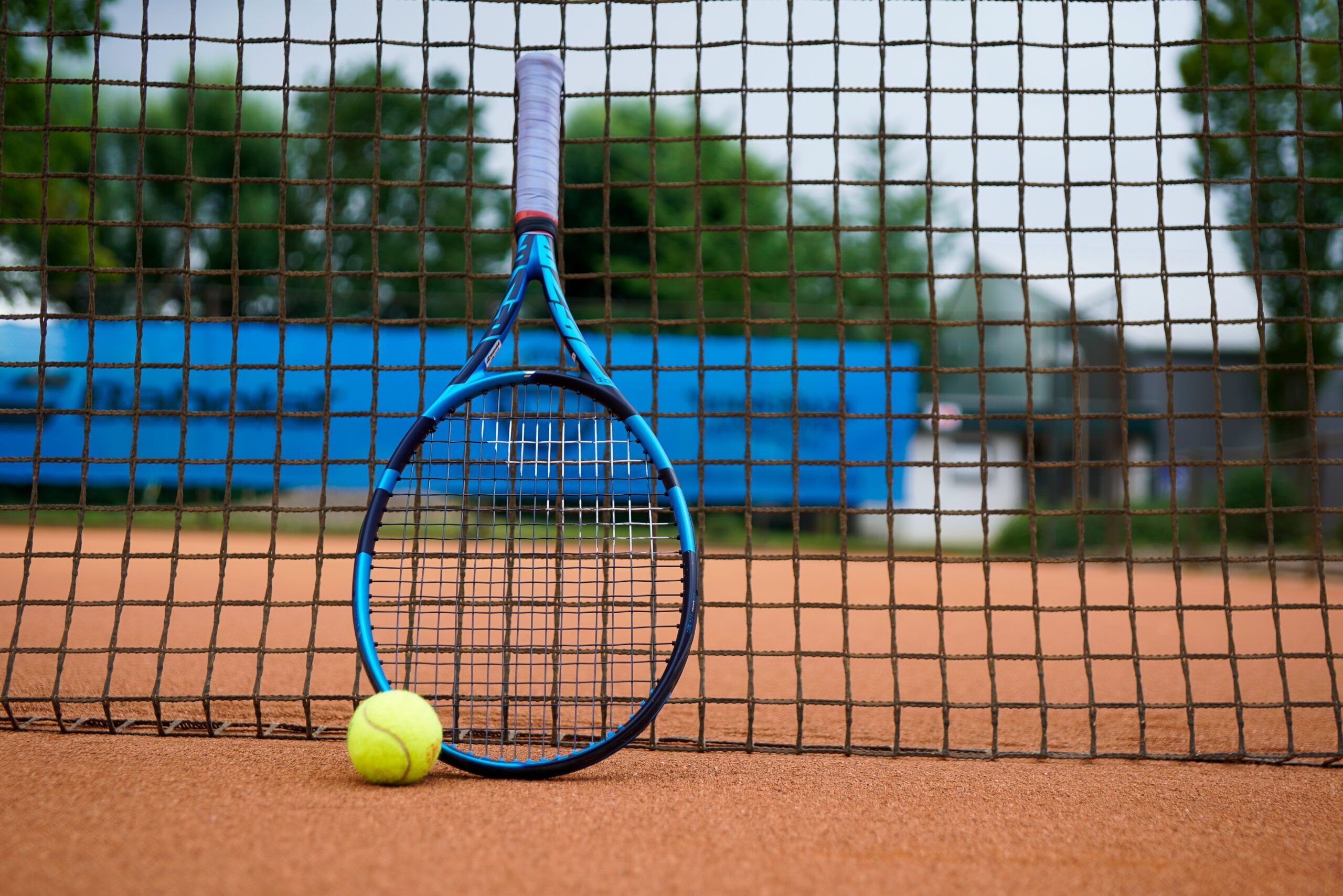 Tennisschläger und Ball am Netz auf Sandplatz