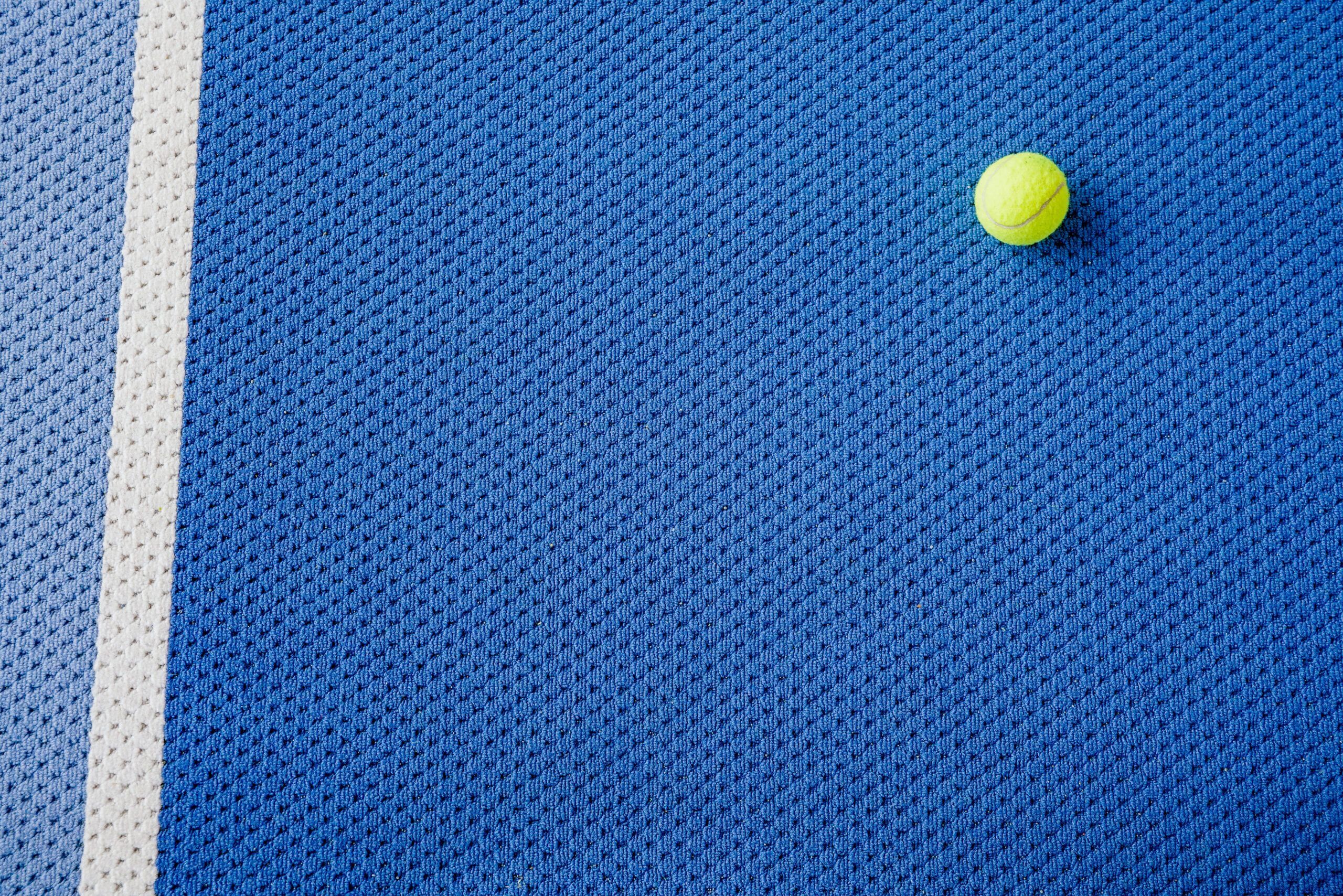 Tennisball auf blauem Tennisplatz neben weißer Linie