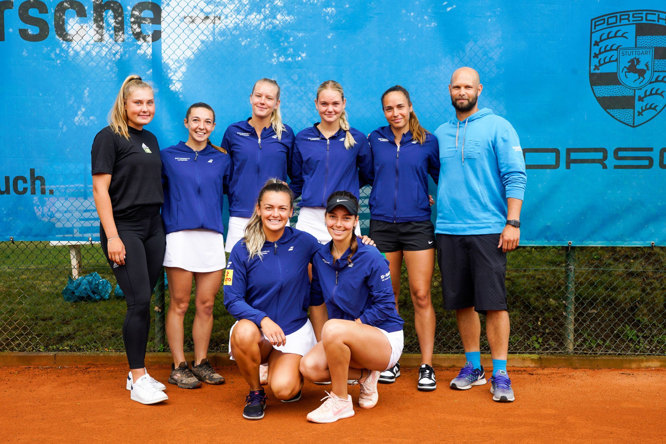 Damentennisteam mit Trainer auf Sandplatz