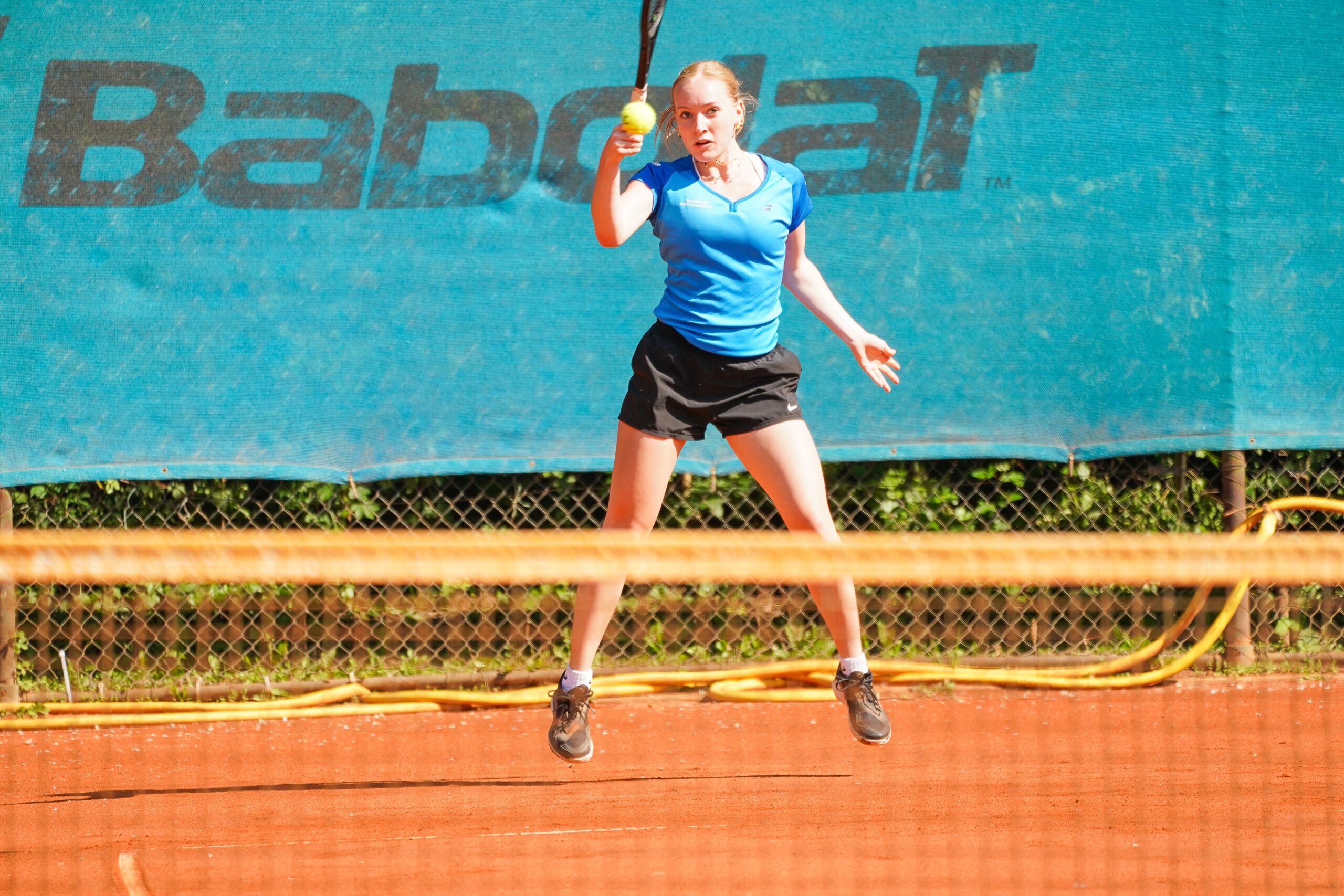 Tennisspielerin schlägt Ball auf Sandplatz