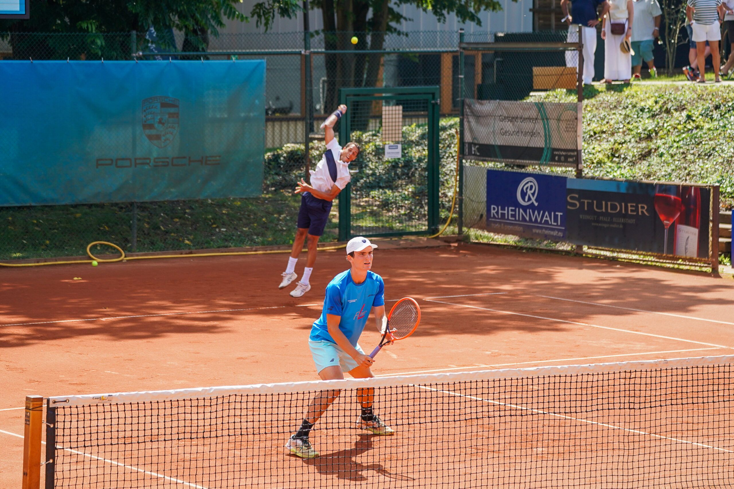 Zwei Tennisspieler auf Sandplatz während Aufschlag