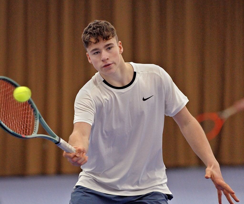 Junger Tennisspieler schlägt Ball in der Halle