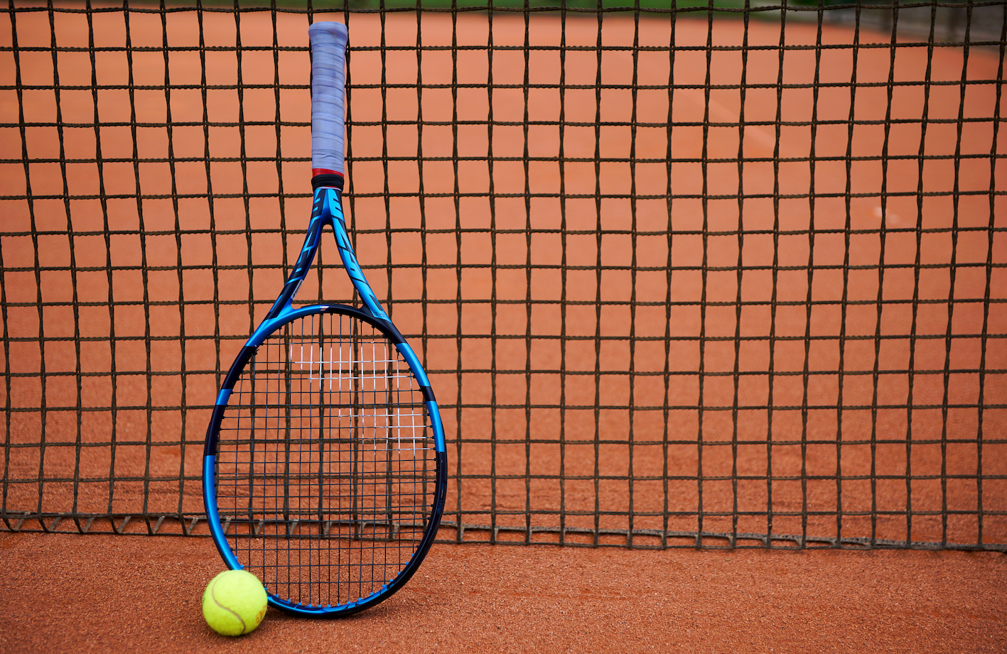 Tennisschläger und Ball vor Netz auf Sandplatz