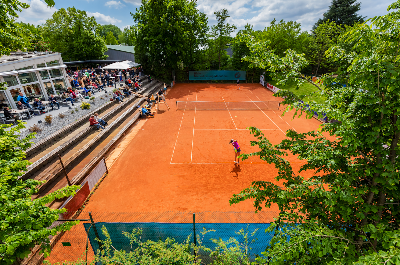 Tennisspiel auf Sandplatz mit Zuschauern im Grünen