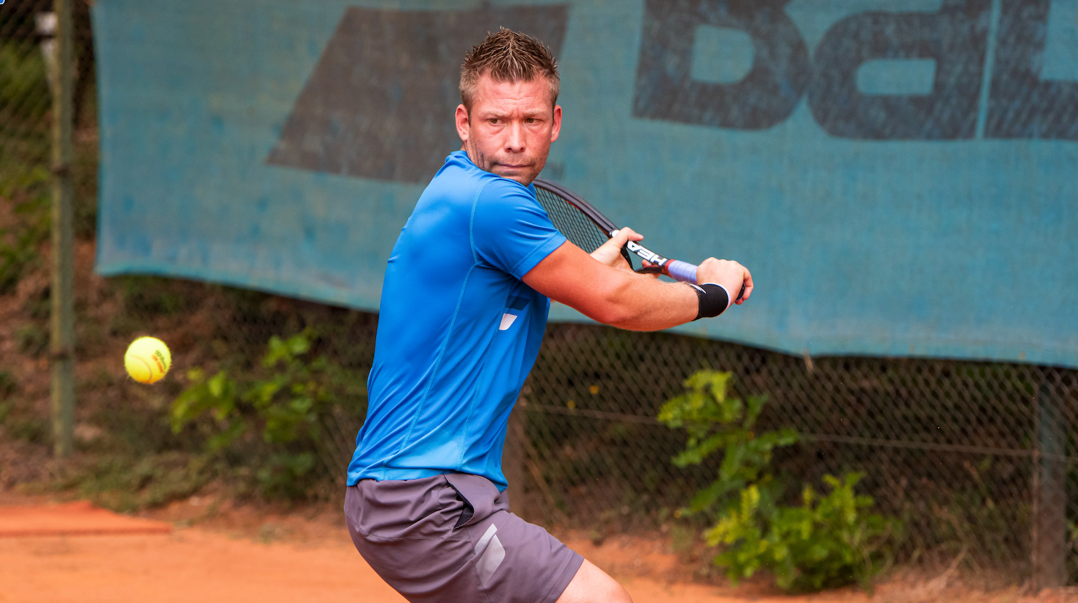 Tennisspieler beim Rückhandschlag auf Sandplatz