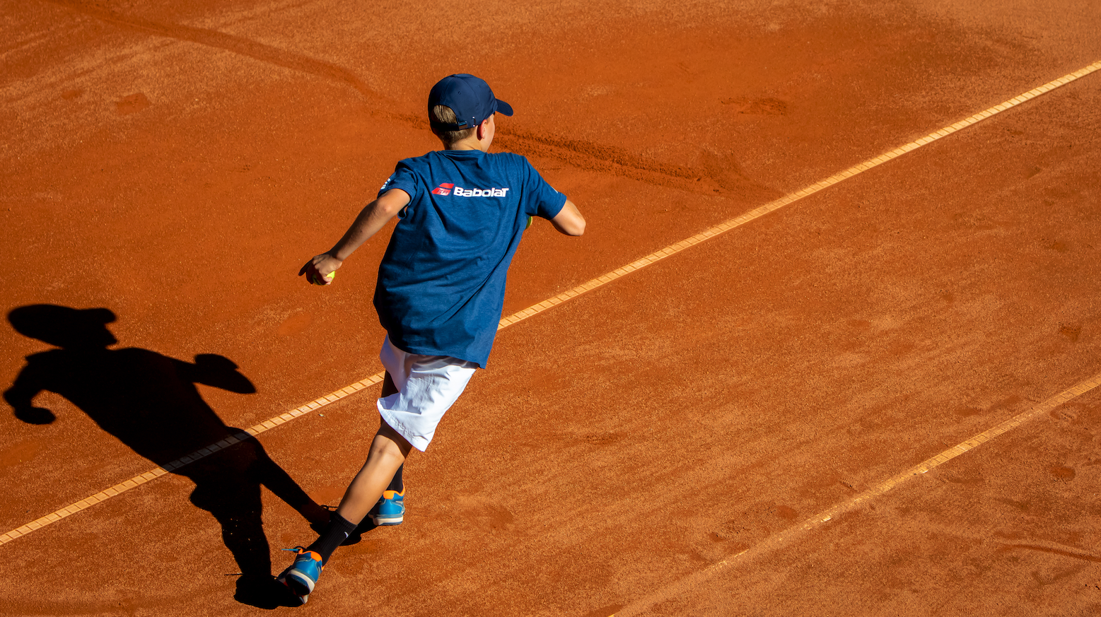 Junge spielt Tennis auf Sandplatz von oben