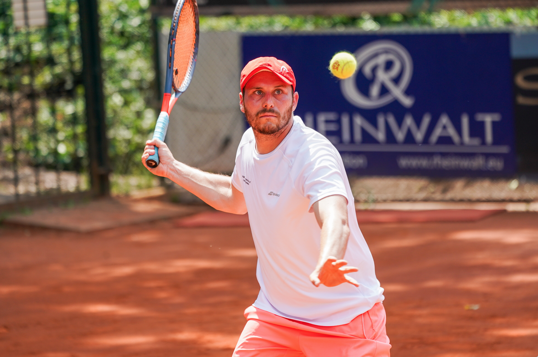 Tennisspieler schlägt Ball auf Sandplatz