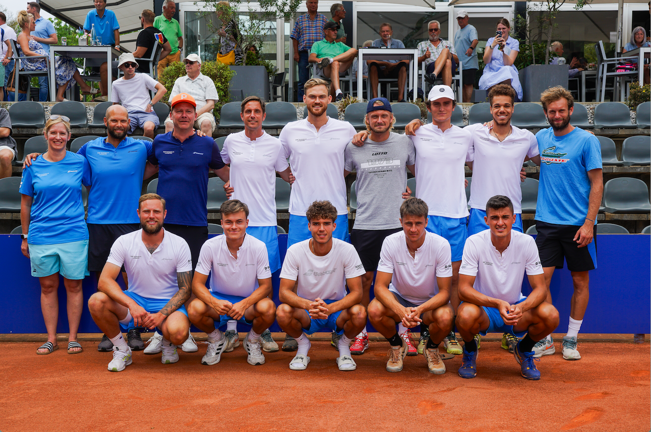 Tennismannschaft posiert auf Sandplatz mit Zuschauern