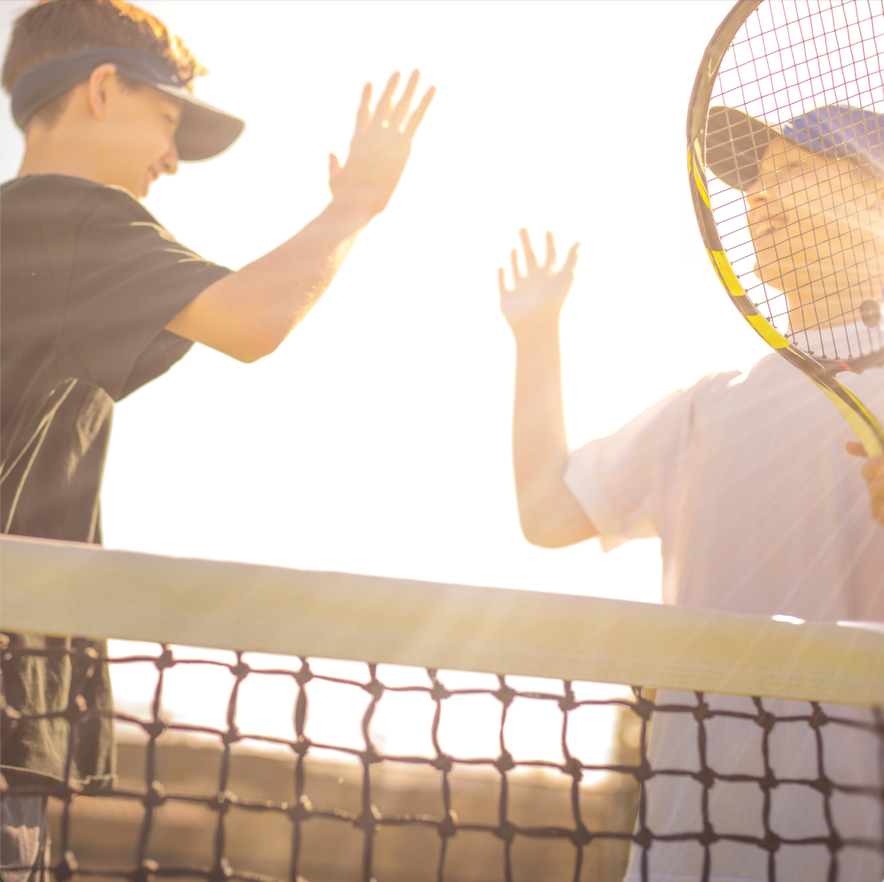 Zwei Jungen geben sich High-Five am Tennisnetz