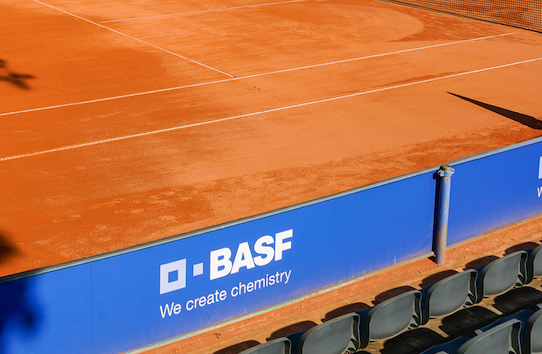 Sand-Tennisplatz mit BASF-Werbebande und leeren Sitzen