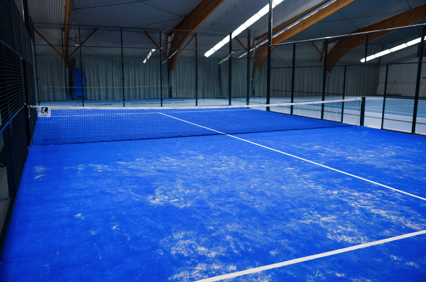 Blauer Indoor-Padelplatz mit Netz und Glaswänden
