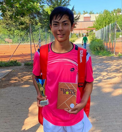 Jugendlicher mit Pokal und Buch auf Tennisplatz