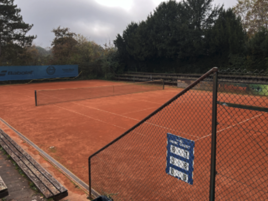 Leerer Sand-Tennisplatz mit Zaun und Bäumen