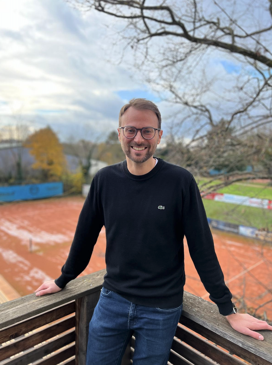 Lächelnder Mann mit Brille vor Tennisplatz