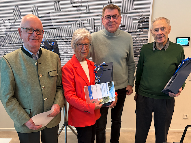 Vier ältere Personen mit Geschenkmappen im Raum