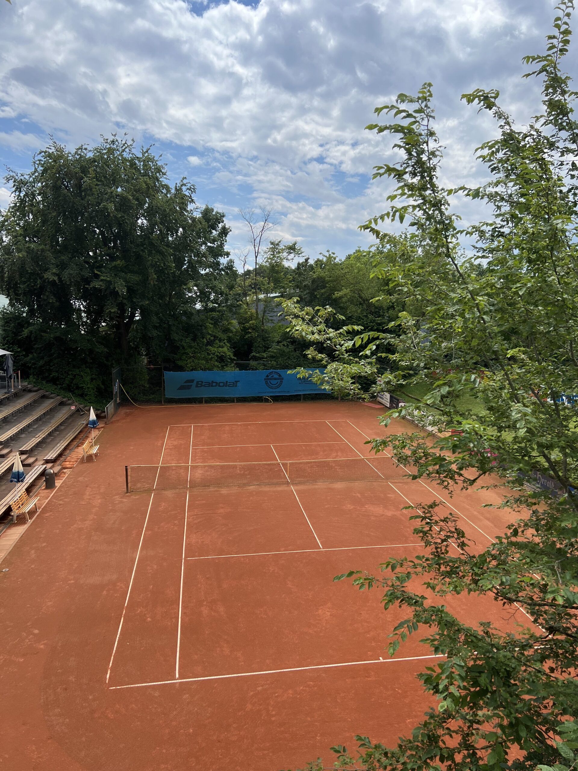 Leerer Sand-Tennisplatz im Grünen unter blauem Himmel