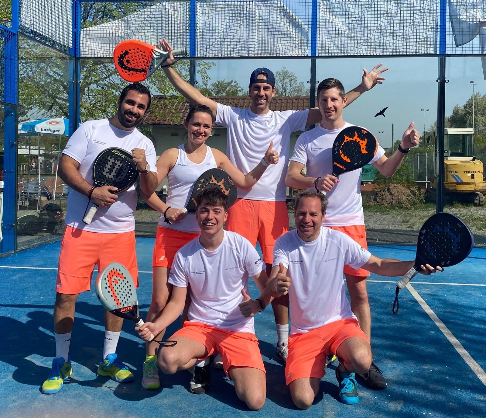 Sechs Padelspieler posieren mit Schlägern auf Court