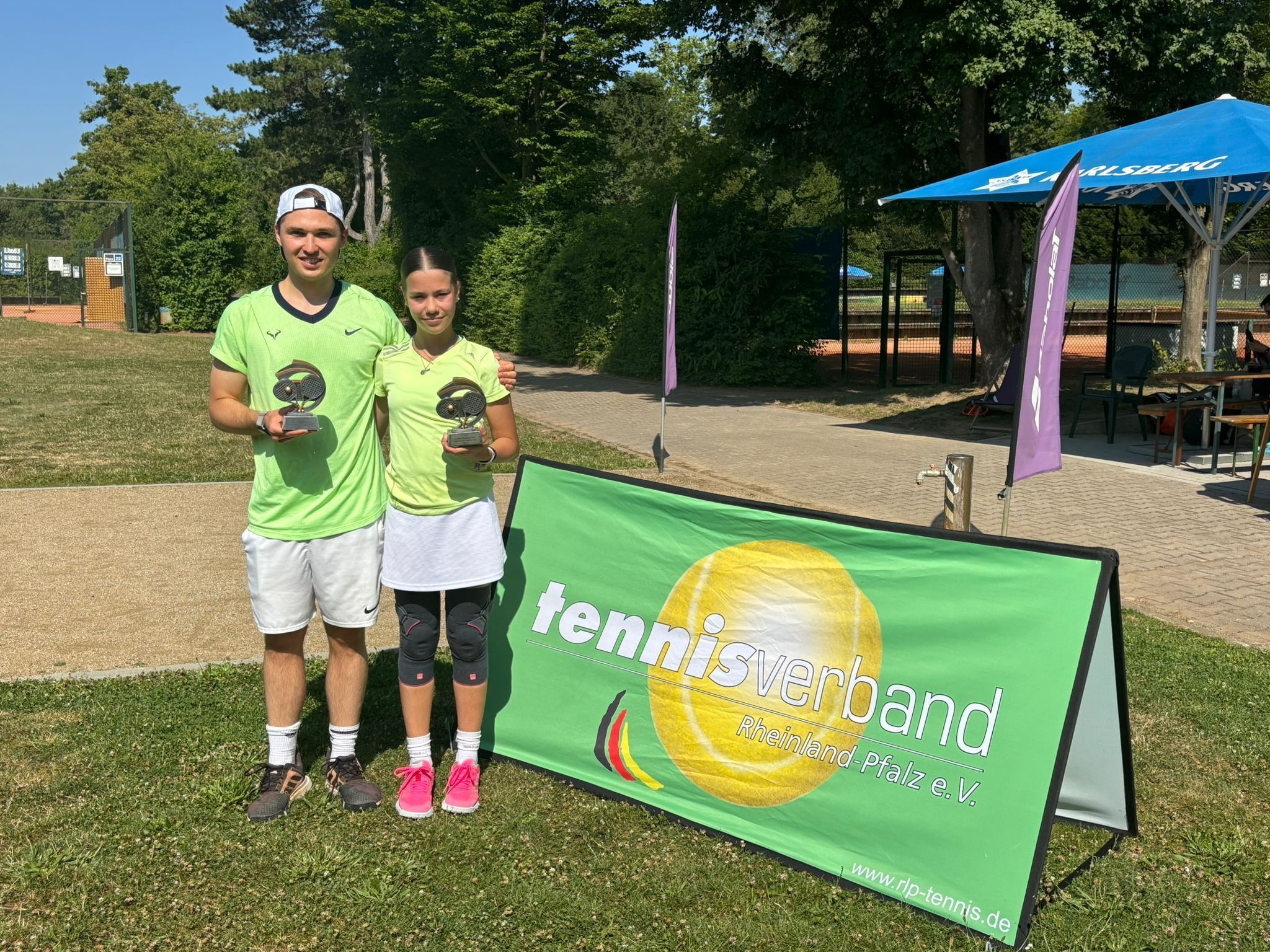 Zwei Tennissieger mit Pokalen auf Tennisplatz