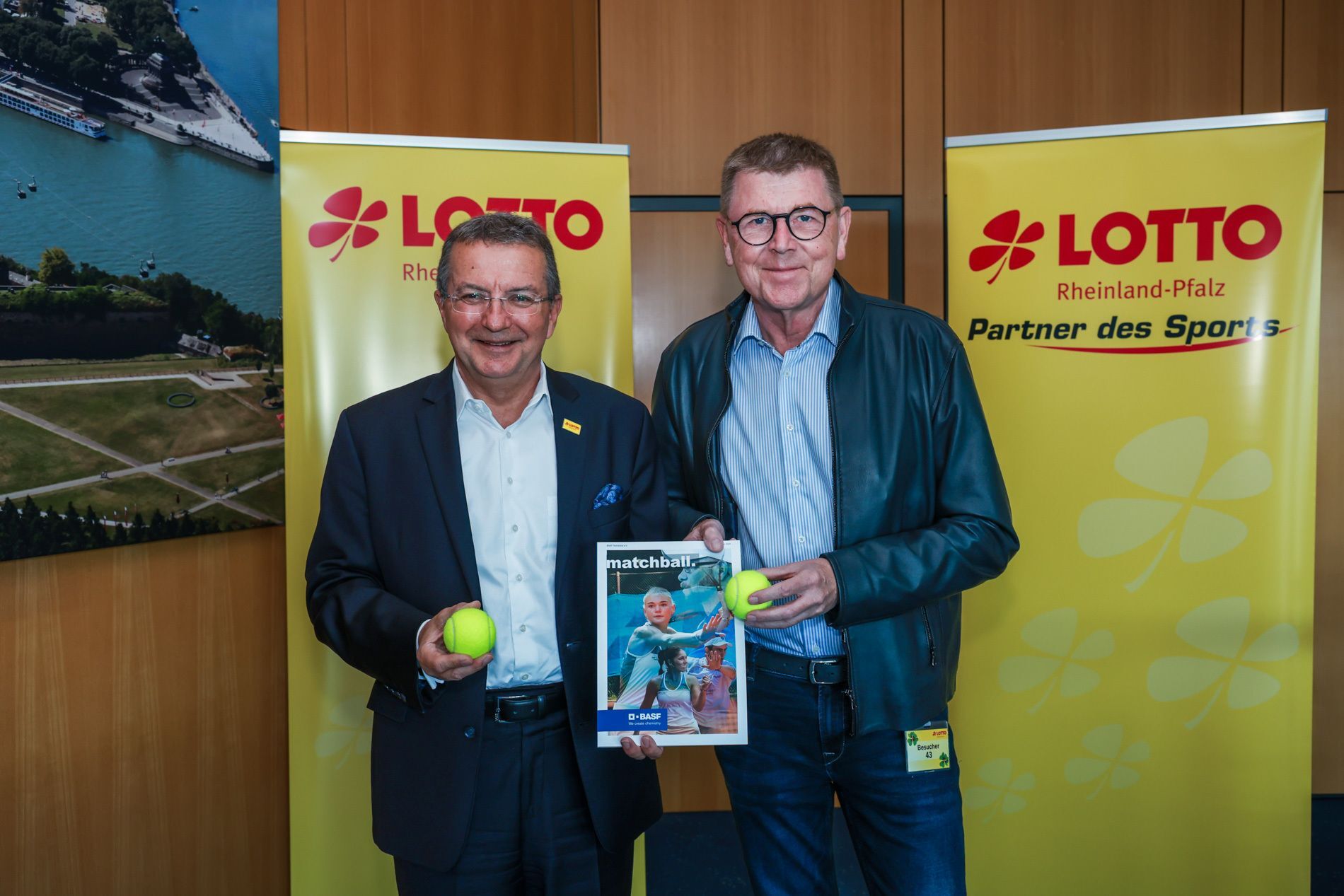 Zwei Männer mit Tennisbällen vor Lotto-Bannern