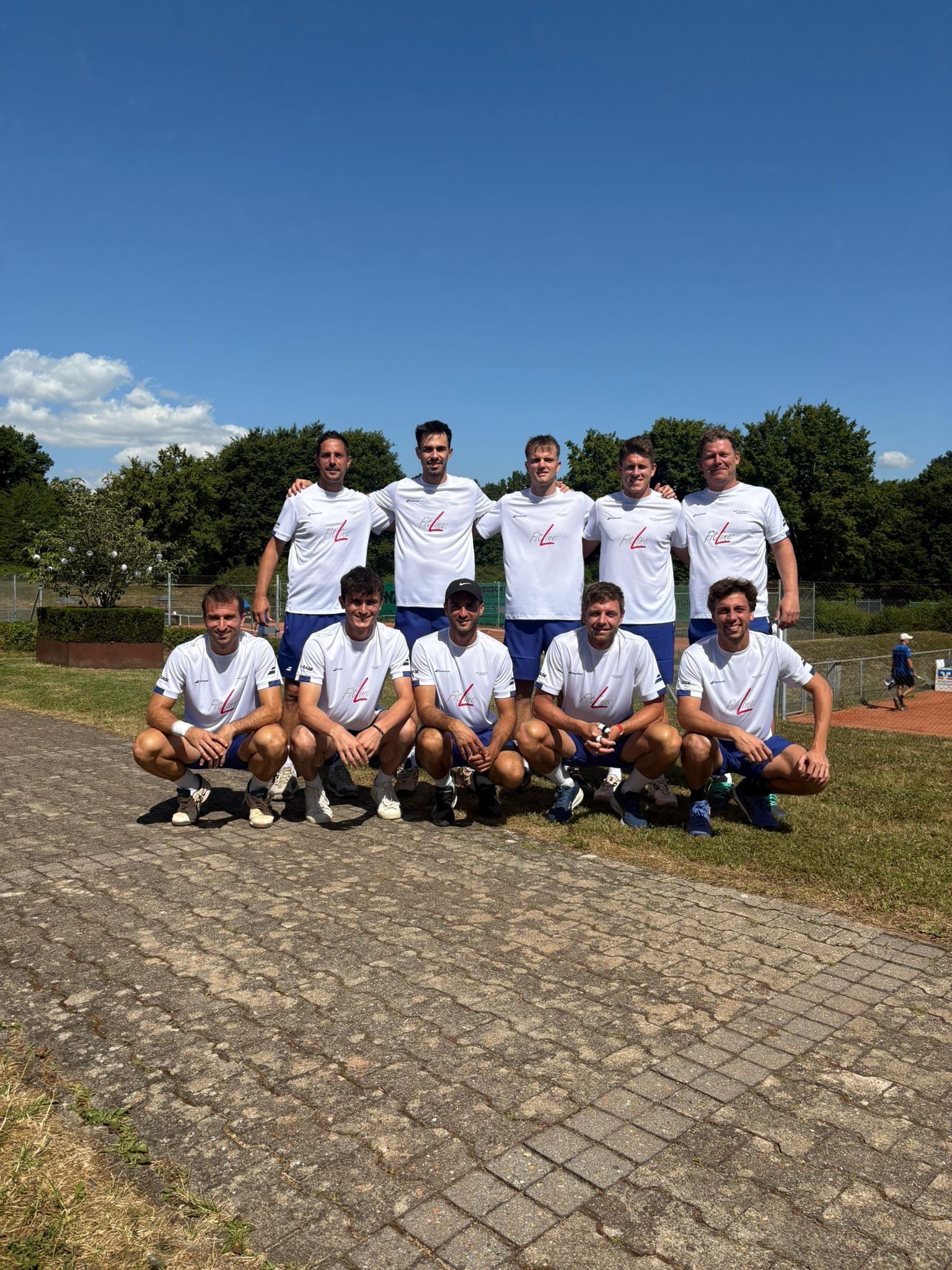 Tennismannschaft posiert auf Außenplatz bei Sonnenschein