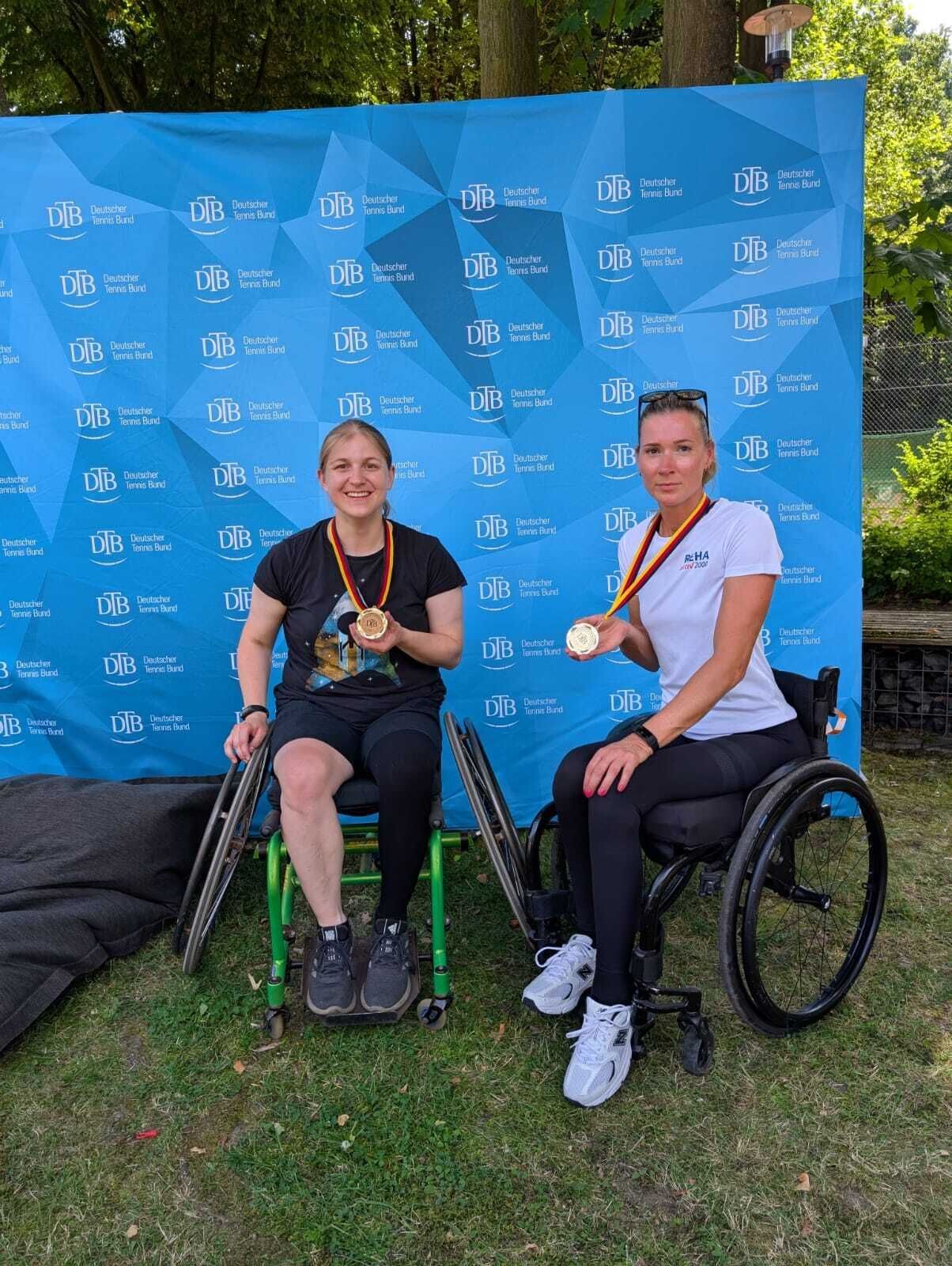 Zwei Rollstuhltennisspielerinnen mit Medaillen vor DTB-Wand