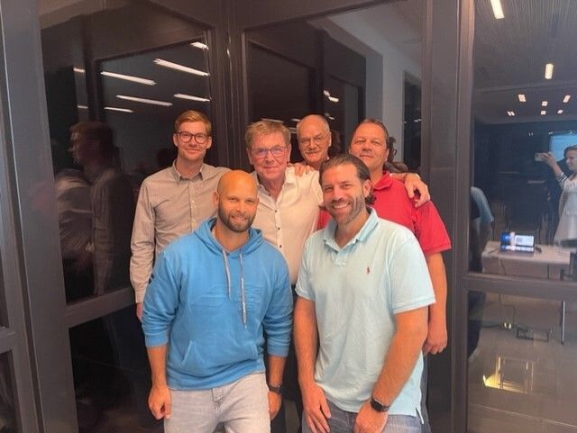 Sechs Männer posieren lächelnd im Büro nachts